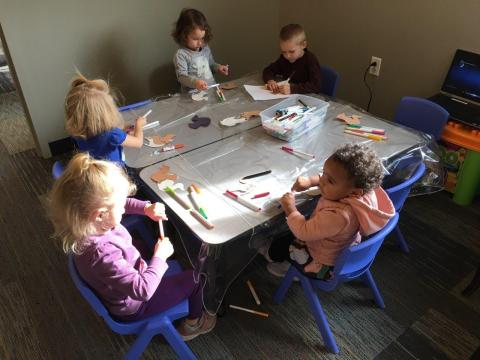 Children sit at small tables working on a paper craft project